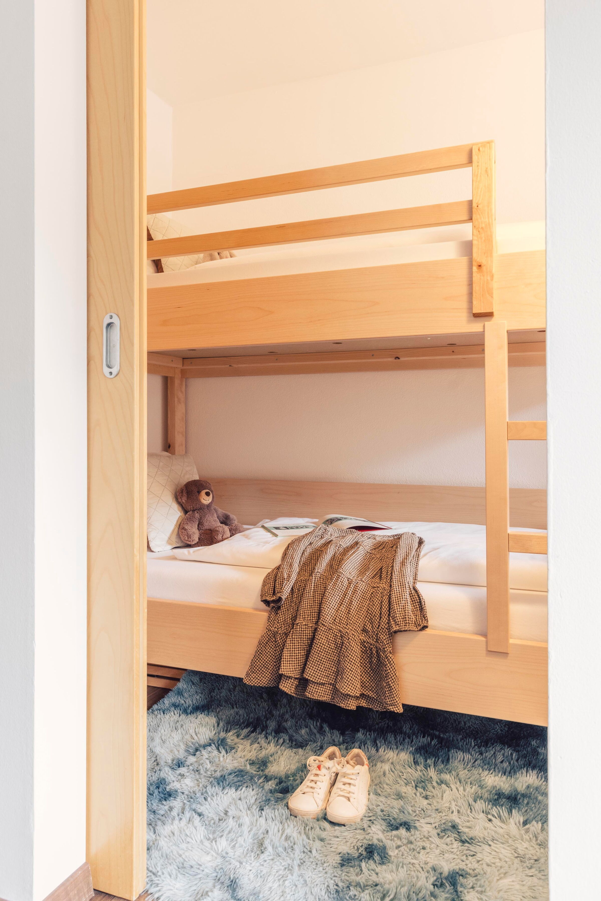 Hochbett aus hellem Holz mit Kuscheltier auf weichem Teppichboden.