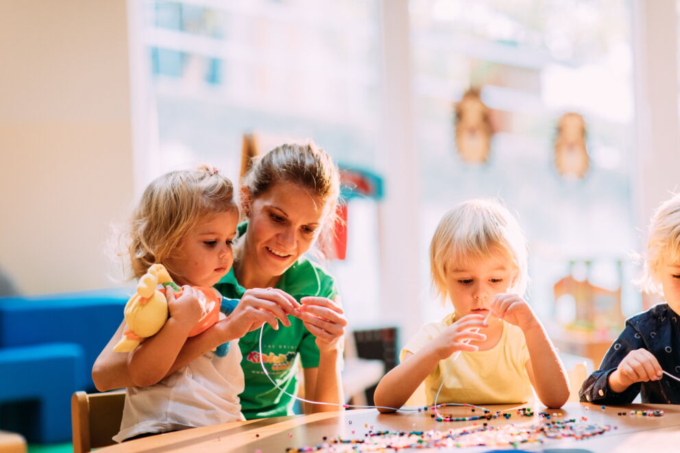 Adults and children work together with beads at the table.