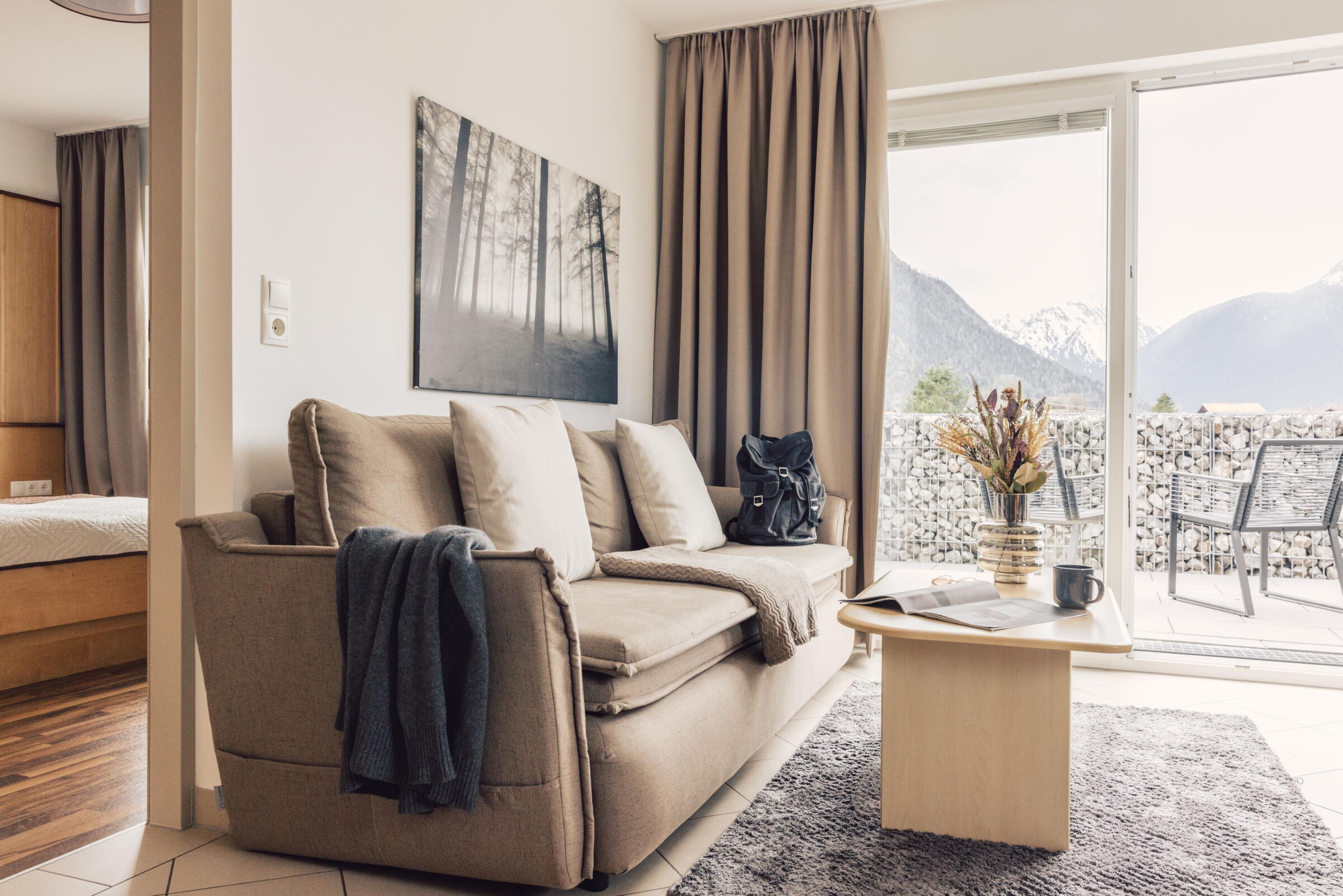 Bright suite with sofa, cushions, table and balcony with mountain view.