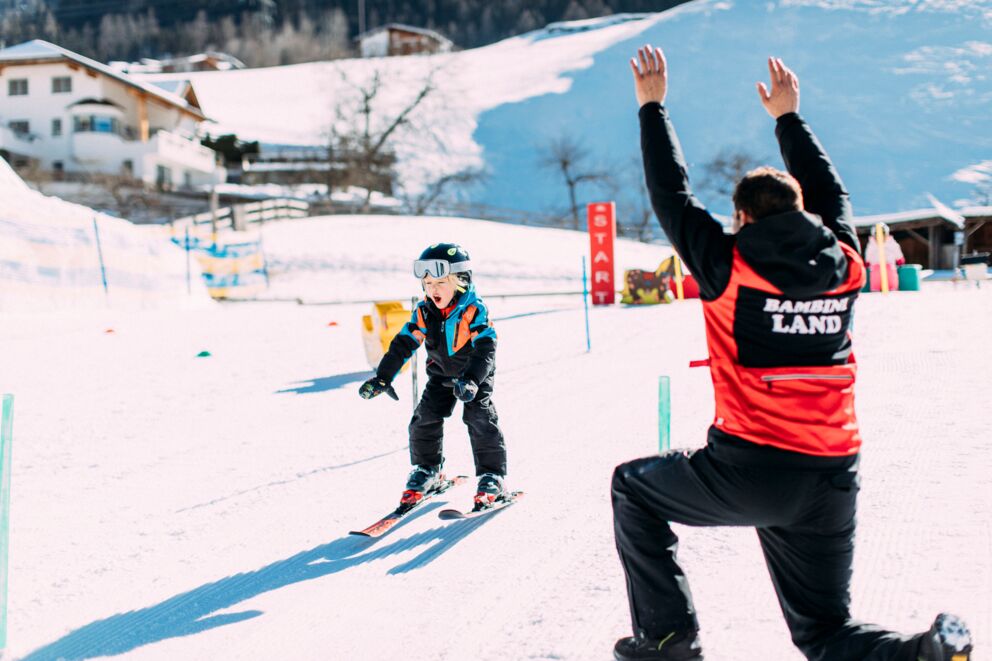 A child gliding down the mountain in the pitztal and a man watch him.