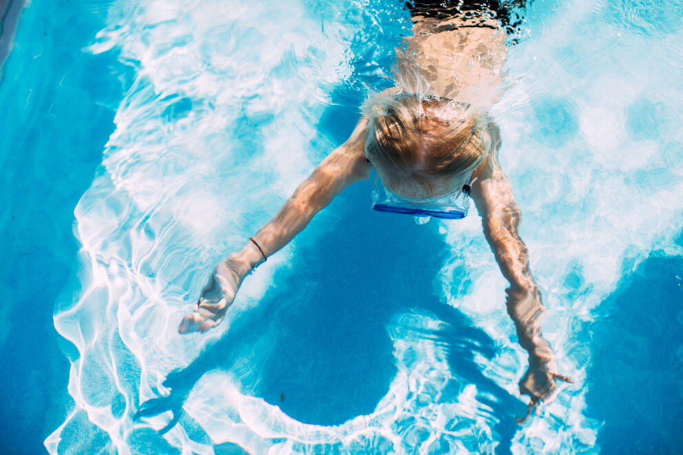 Kind mit Taucherbrille schwimmt im blauen Wasser eines Pools.