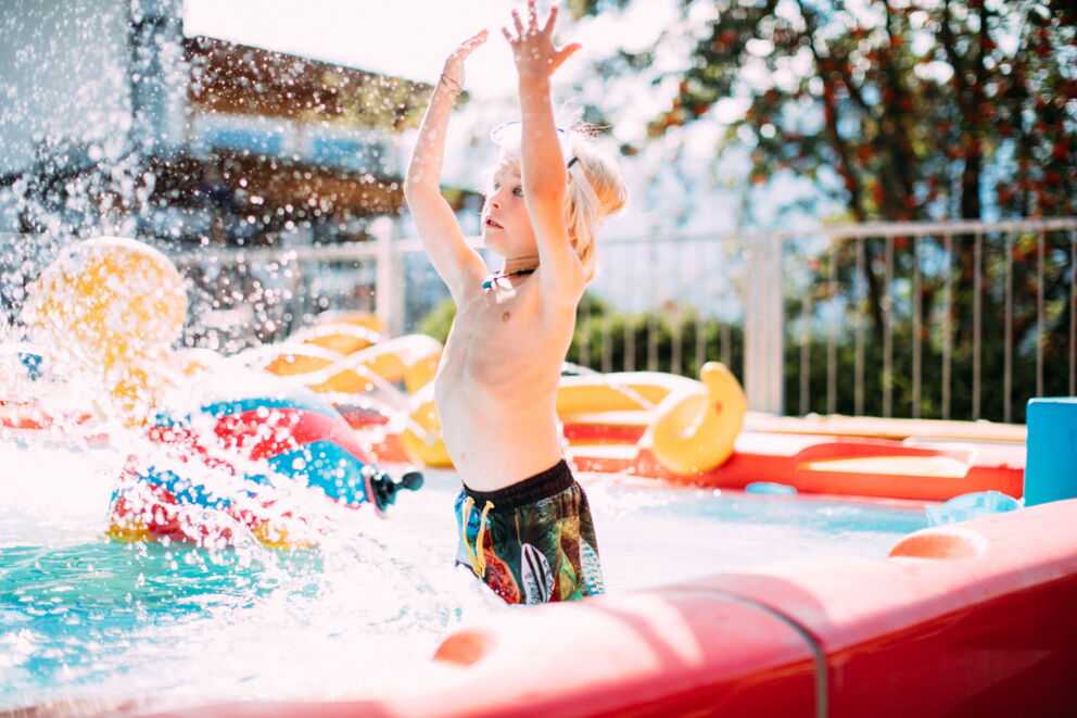 Junge spielt im Wasser, spritzt fröhlich mit Spielzeug in Pool.