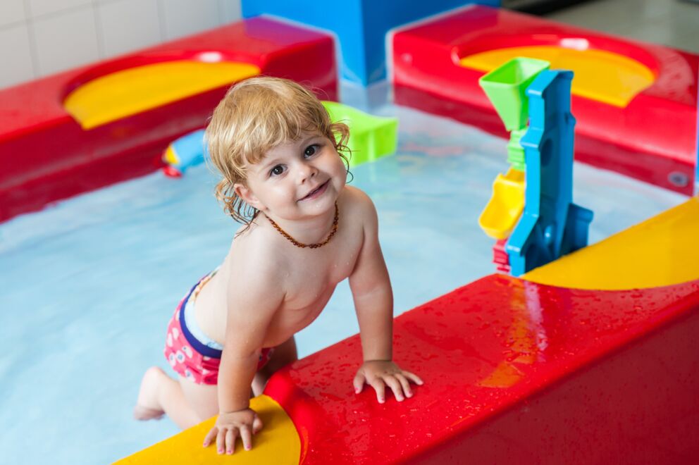 Kleinkind am bunten Wasserspielplatz im Kinderhotel in Tirol.