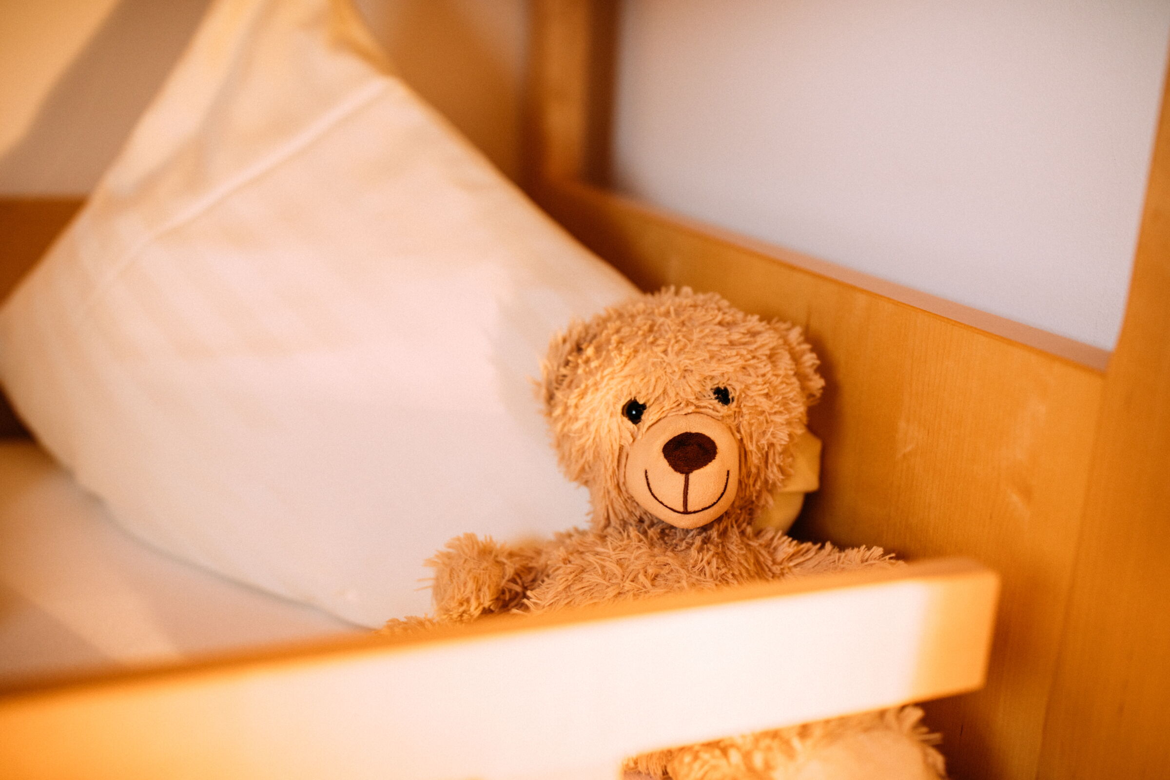 A smiling teddy bear sits next to a soft pillow in a cozy bed.