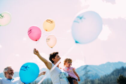 Family with colorful balloons in front of an impressive mountain backdrop on a sunny day.