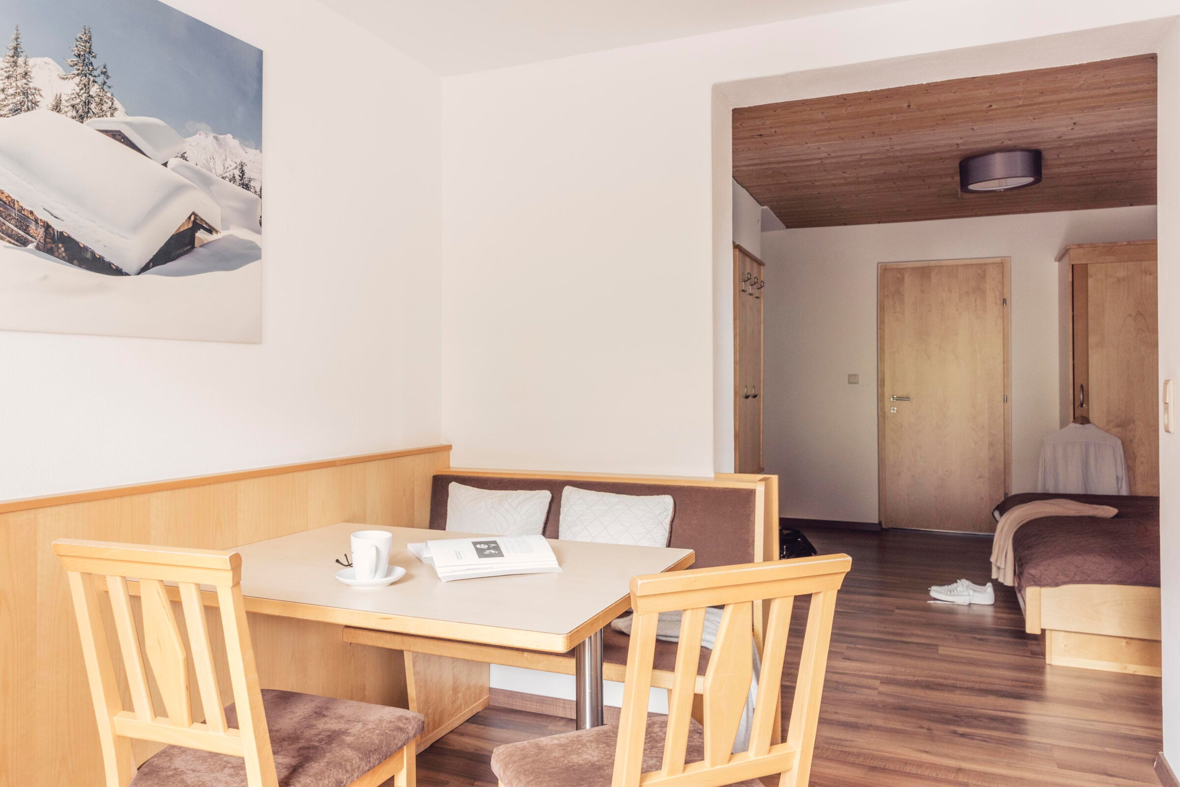 Heller Raum mit Sitzgruppe und einem Bild von verschneiten Bergen an der Wand.
