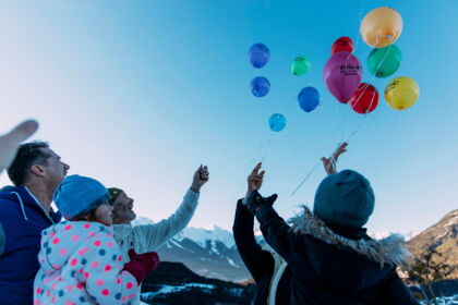 Familien lassen bunte Ballons in klarer Bergluft steigen, umgeben von majestätischen Alpen.
