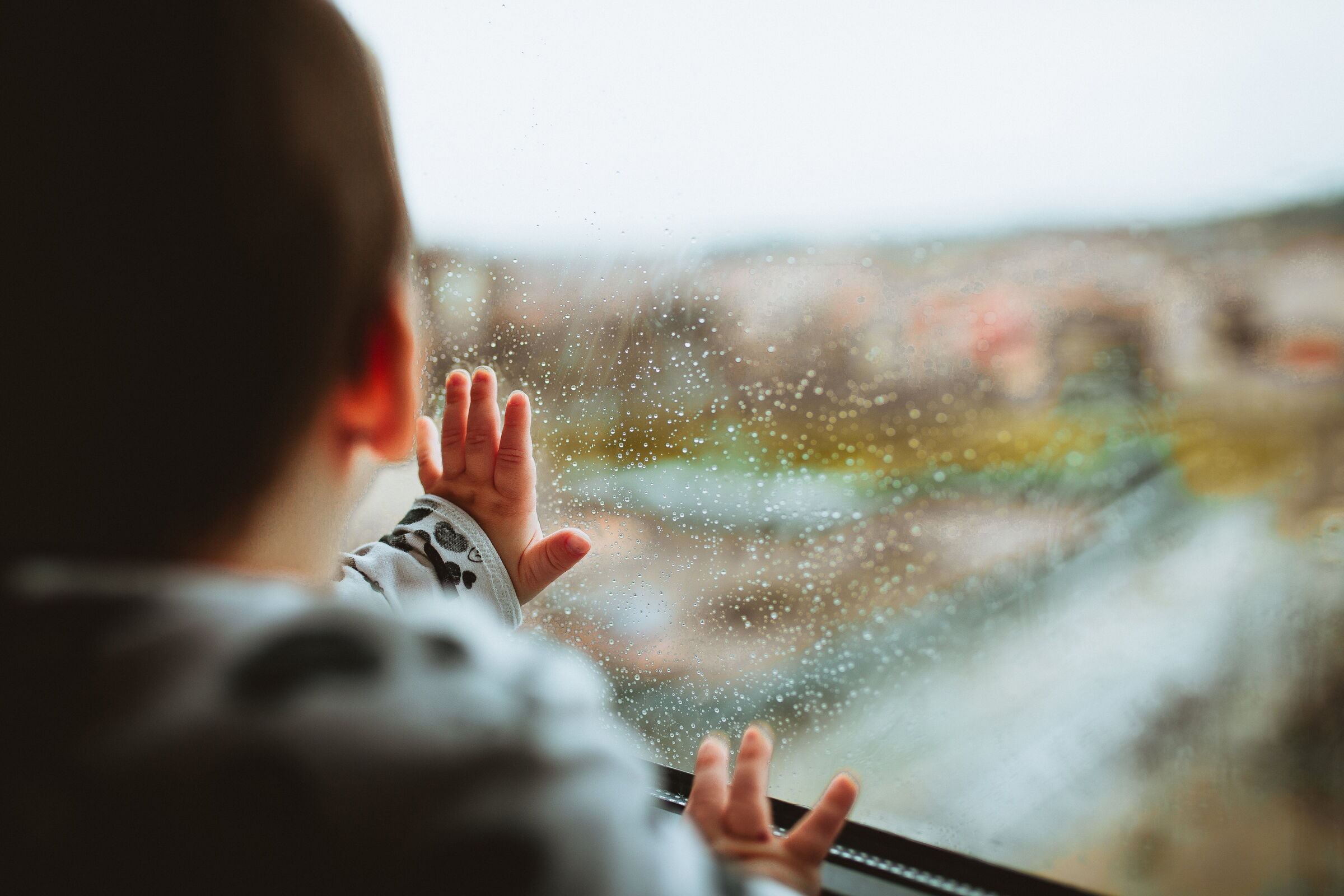 A baby looks out of a rainy window into a blurred winter landscape.