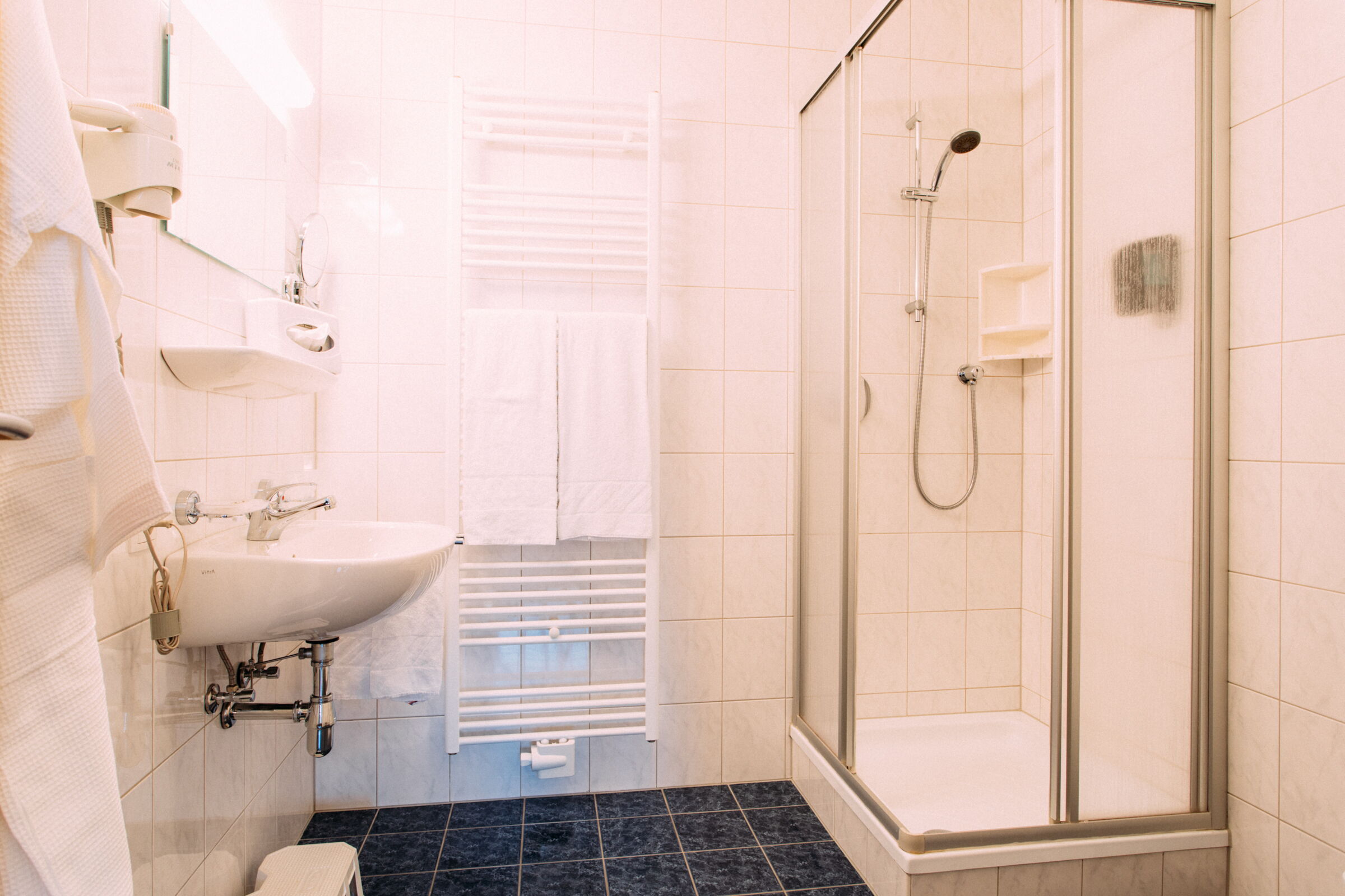 Bright bathroom with shower, washbasin, towel rail and white tiles.