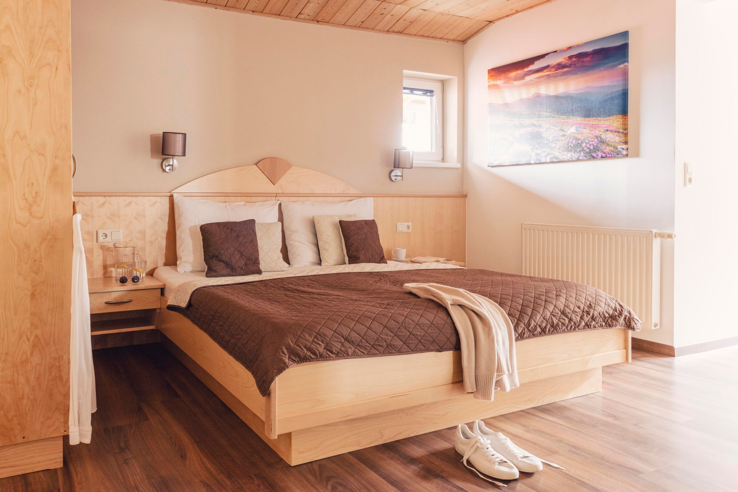 Helles Zimmer mit Doppelbett, Holzmöbeln, Wandkunst und natürlichem Licht.