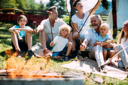 Familie grillt Marshmallows am Lagerfeuer in sonniger Tiroler Umgebung.