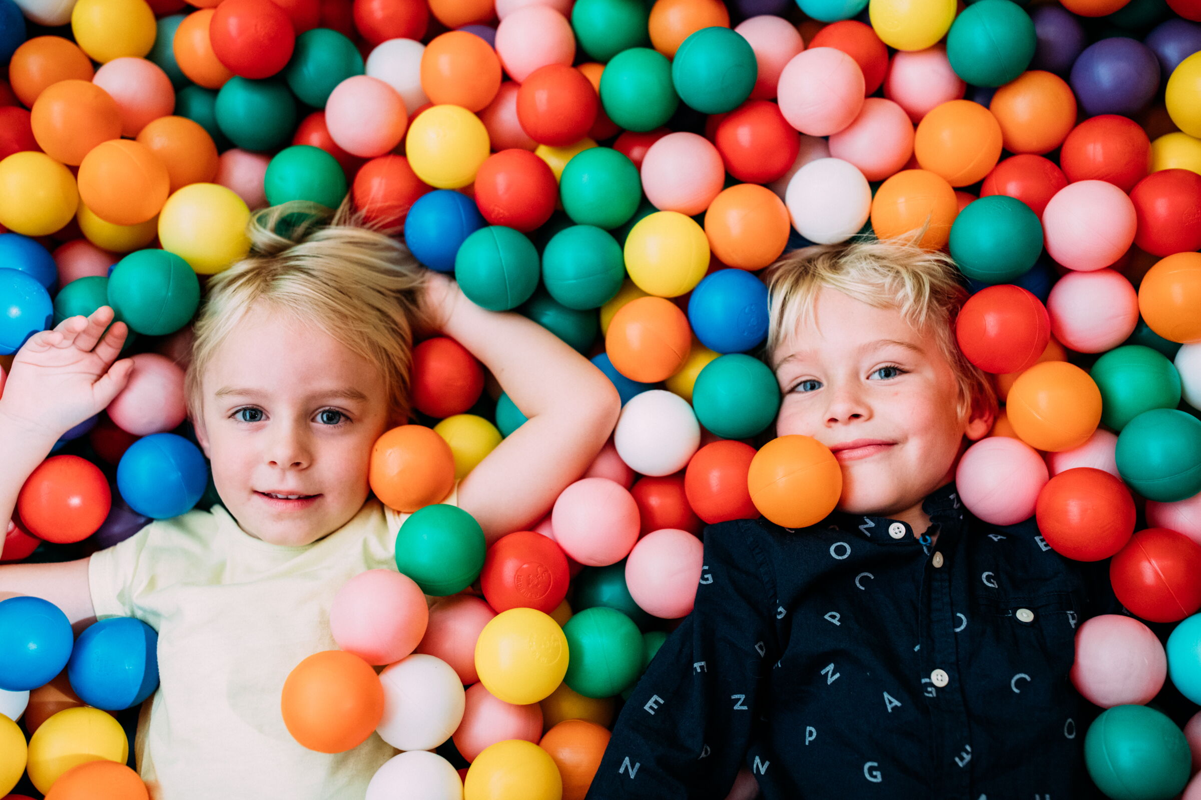 Two children lie happily in the colorful ball pool and smile.