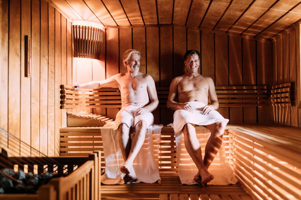 Zwei Männer entspannen in einer warmen Sauna mit Holzverkleidung.