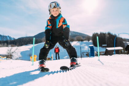 Kind in Skiausrüstung auf sonniger Piste, lächelnd und bereit für Abenteuer.