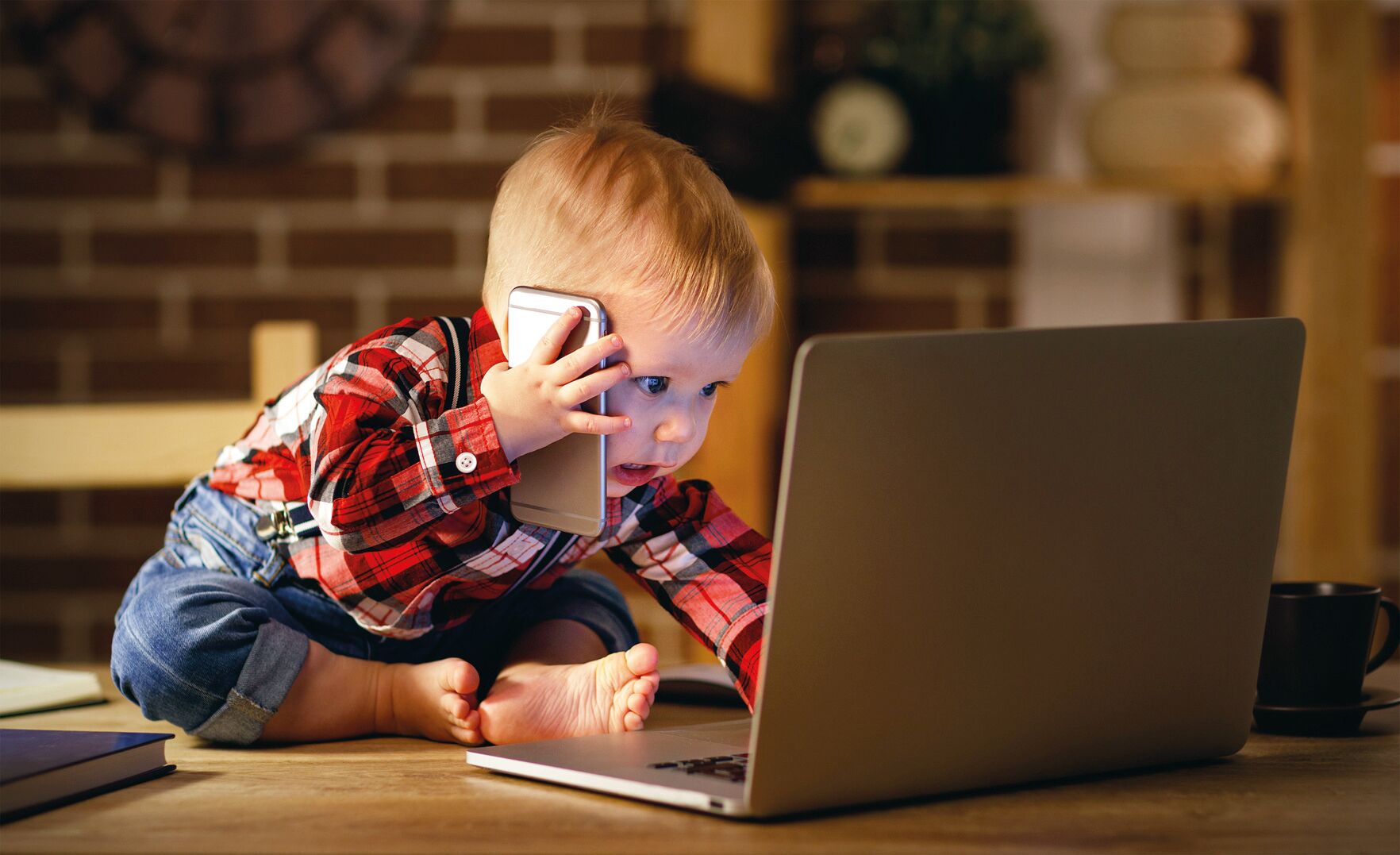 Kleinkind mit Handy und Laptop, in Jeans und kariertem Hemd