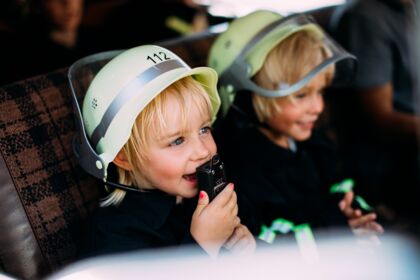 Zwei Kinder in Feuerwehrhelmen lachen und spielen im Pitzis Kinderhotel.