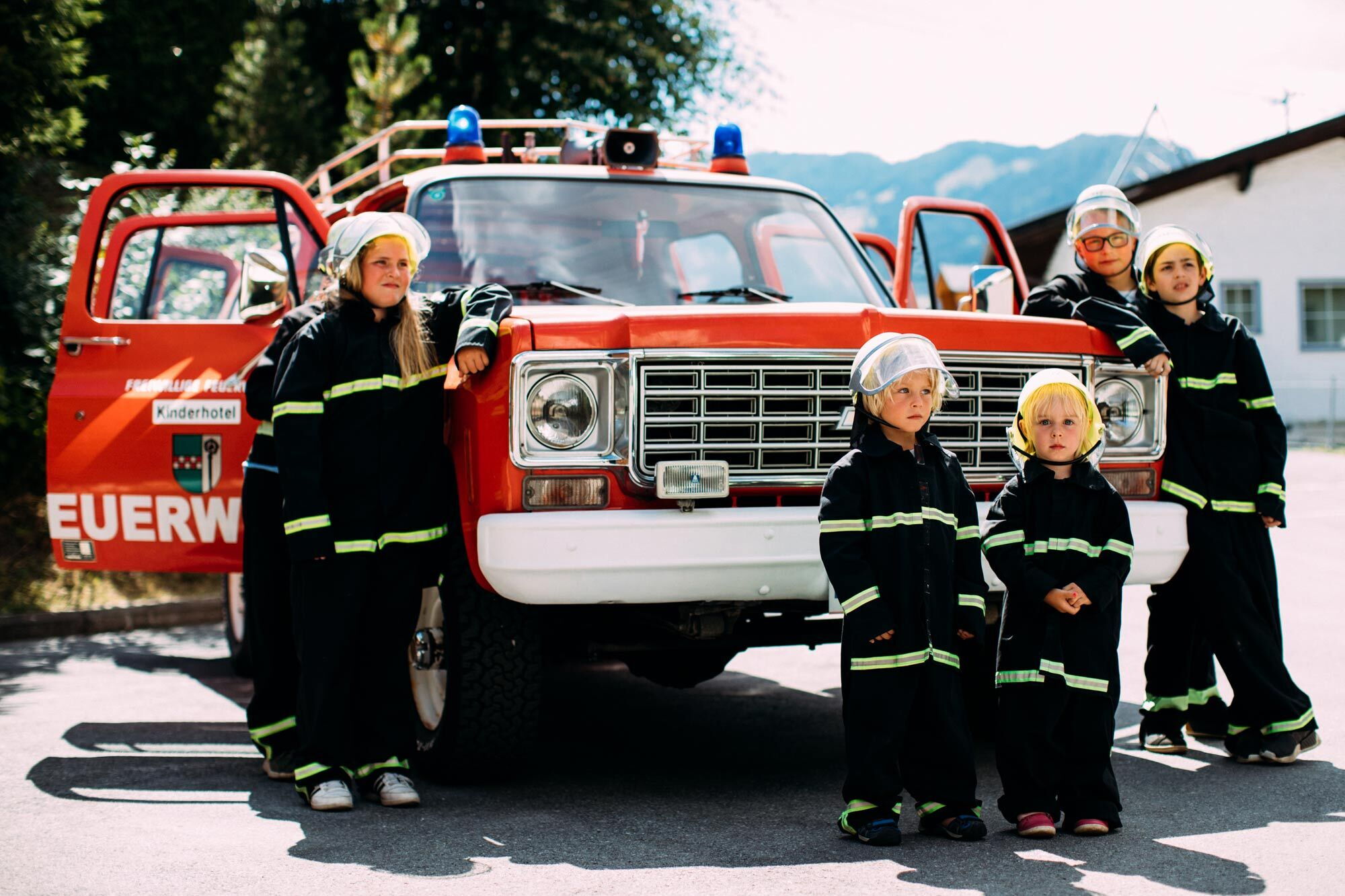 Kinder in Feuerwehrkleidung vor rotem Feuerwehrauto, bereit für Abenteuer.