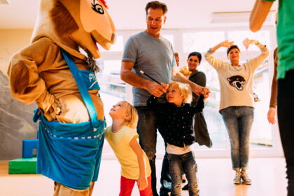 Kinder lachen mit einem Maskottchen in einem hellen Raum voller Freude.