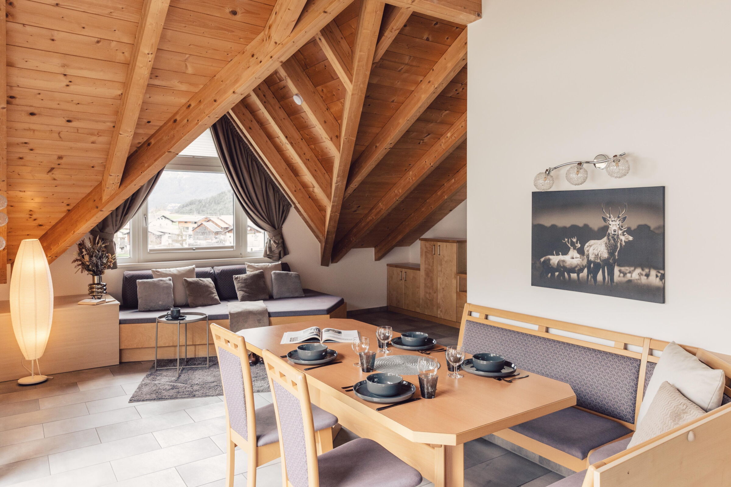 Gemütliches Zimmer mit Holzdach, bequemen Sofas, Esstisch und Bergblick.