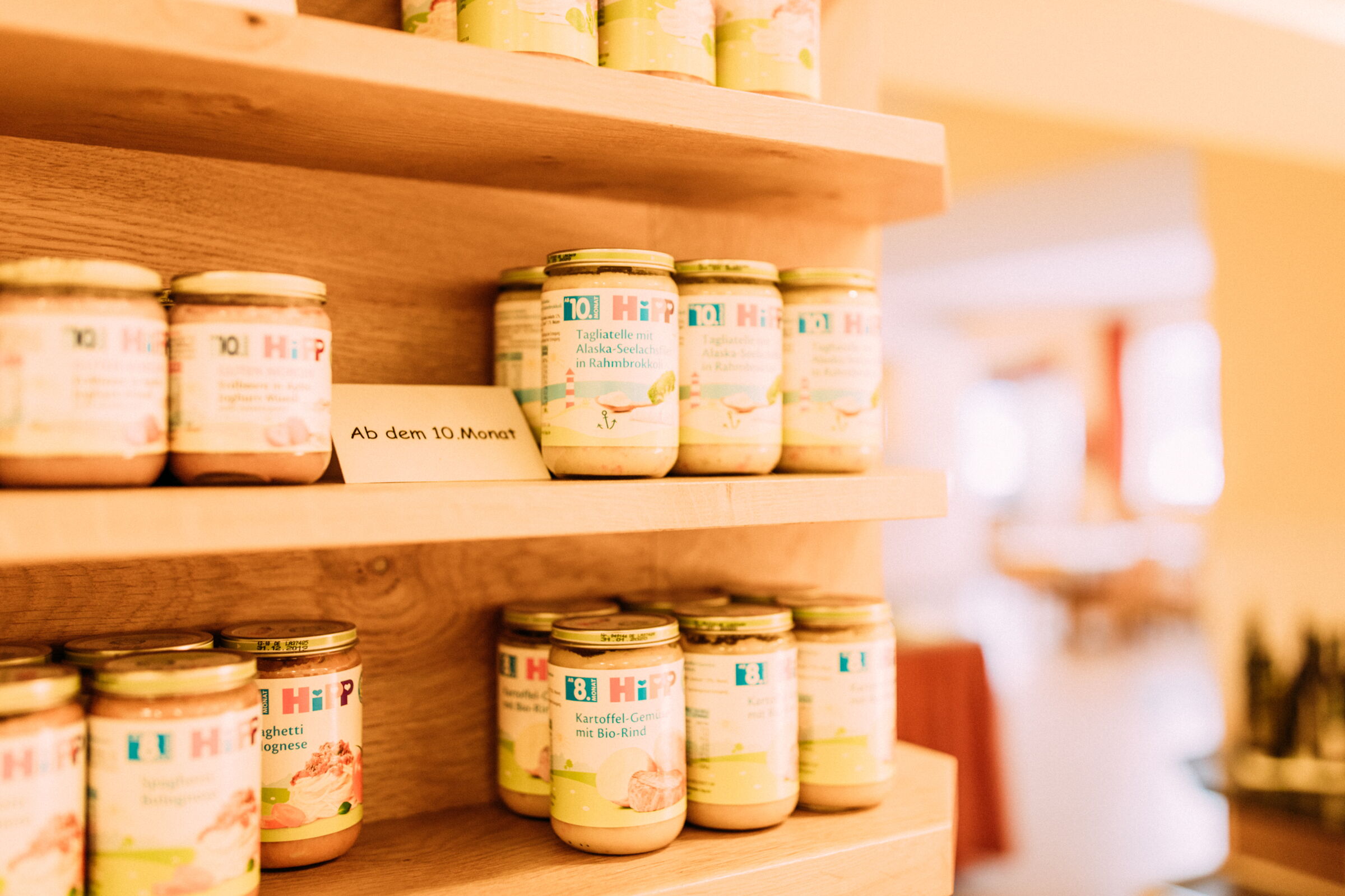 Jars of baby food presented on wooden shelves in warm light.
