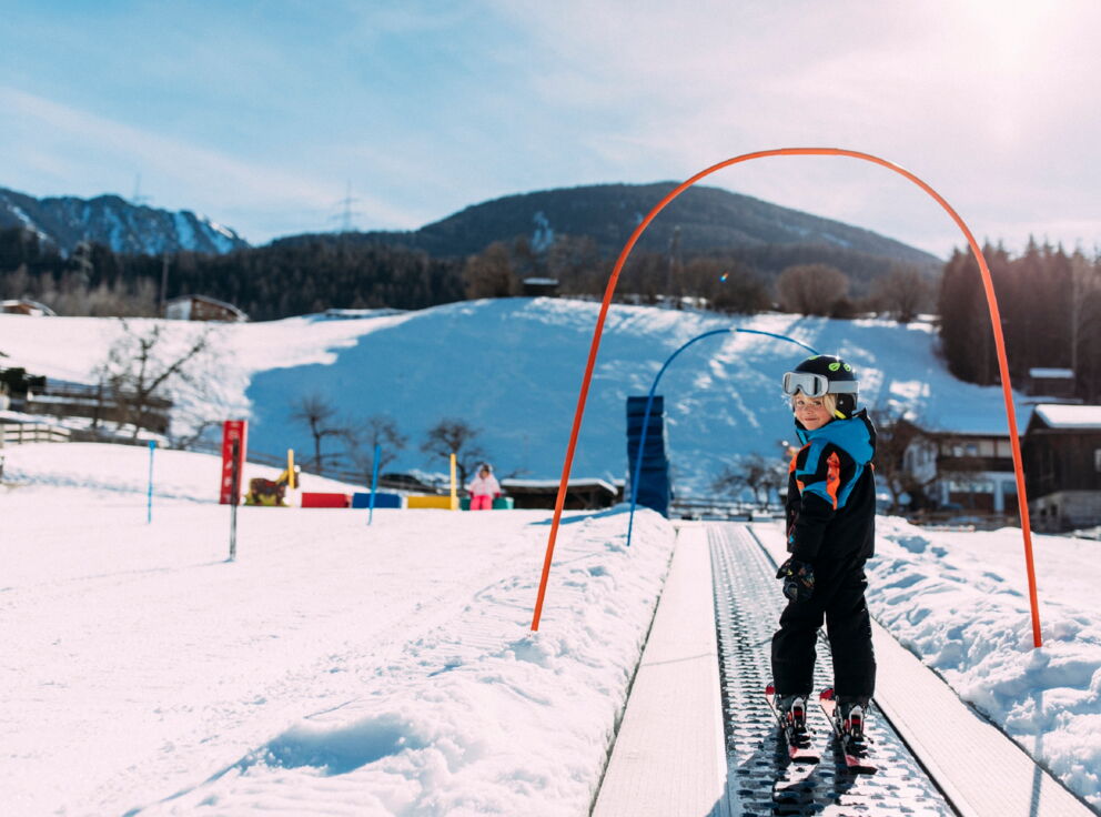 Child on skis on a conveyor belt in a snowy ski resort.