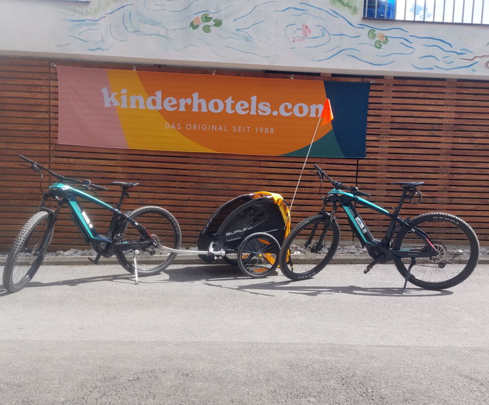 Two bicycles with child trailers positioned in front of an advertising banner.