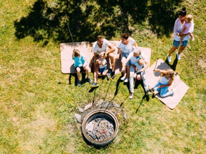 Familien sitzen auf Decken um ein Lagerfeuer, genießen gemeinsam die Natur.