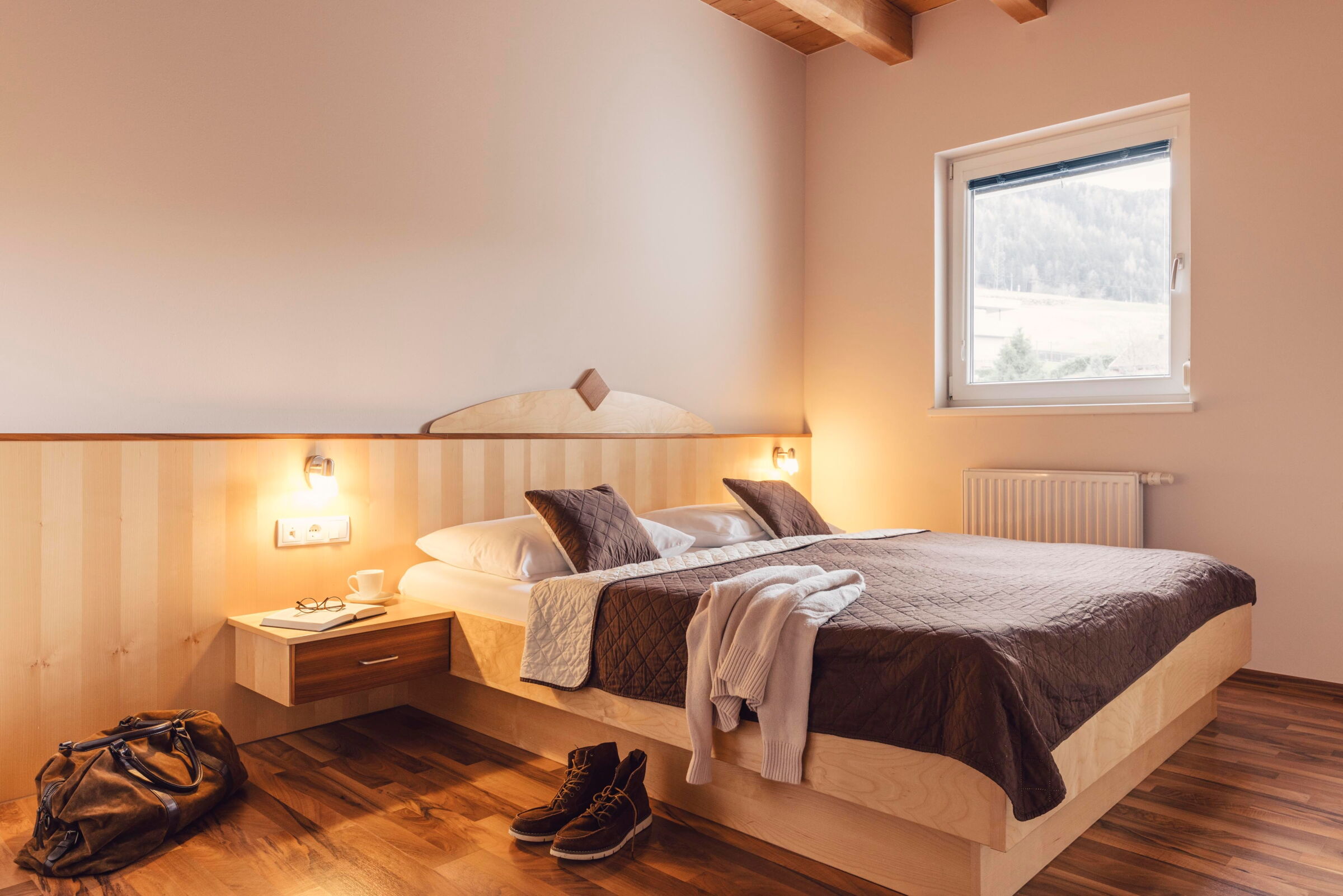 Helles Schlafzimmer mit Holzmöbeln, Bett und Fenster mit Bergblick.