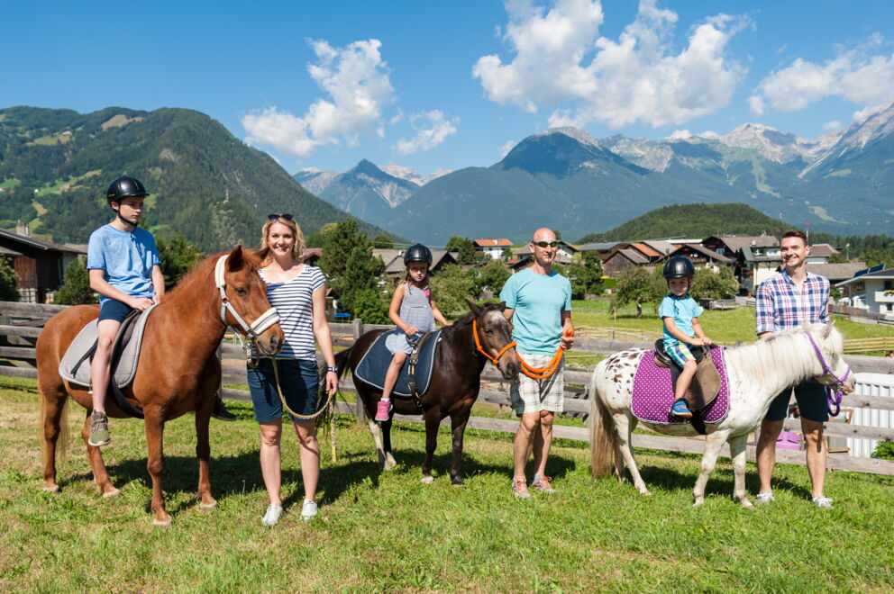 Familien genießen Reitspaß vor beeindruckender Bergkulisse in Tirols Sonne.