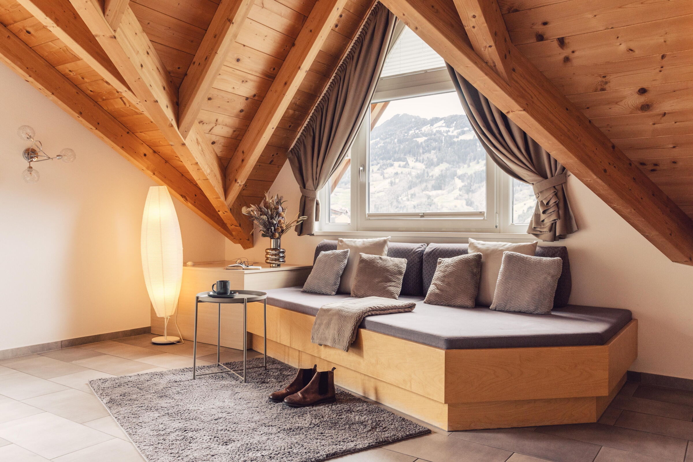Sonnendurchflutete Sitzecke mit Holzdecke, Kissen, Fensterblick und Lampe.