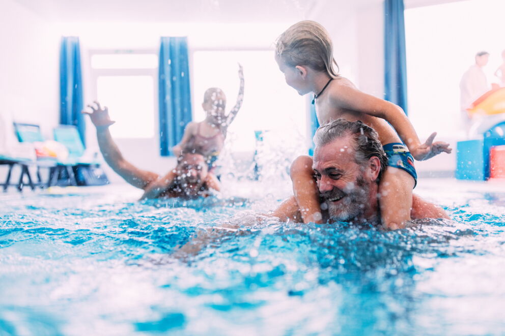 Adults and children play happily in the hotel pool with splashing water.
