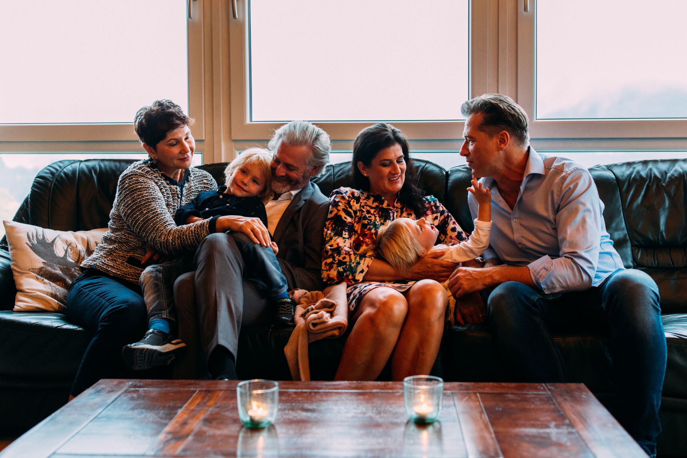 Family relaxing smiling on sofa in front of large window, cozy atmosphere