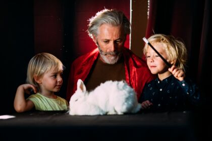 Two children and a magician with a white rabbit on the table.
