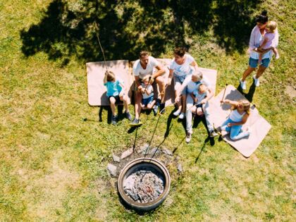Familien sitzen auf Decken um ein Lagerfeuer, genießen gemeinsam die Natur.