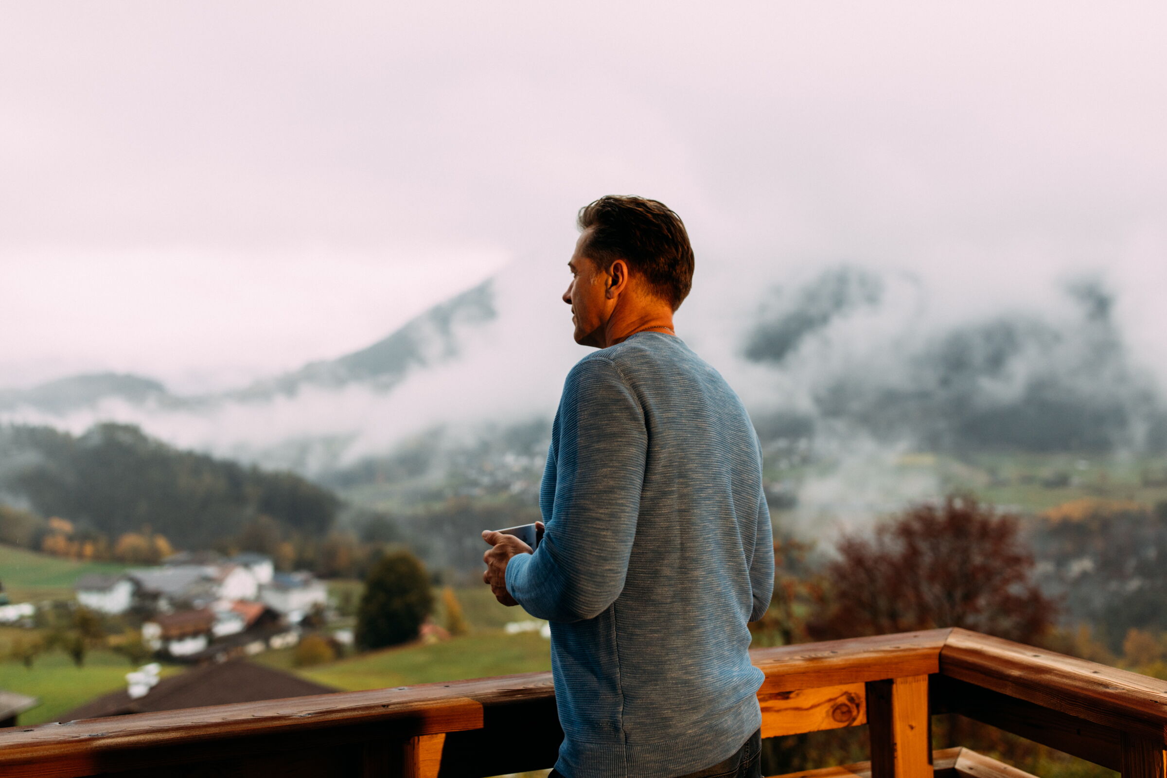 Mann auf Balkon genießt neblige Berglandschaft im Morgengrauen