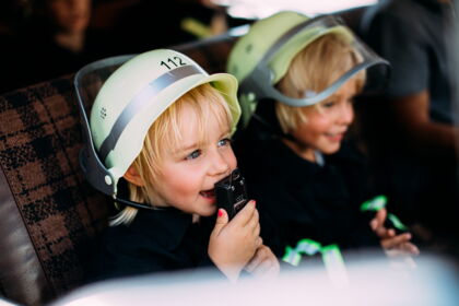 Zwei Kinder in Feuerwehrhelmen lachen und spielen im Pitzis Kinderhotel.
