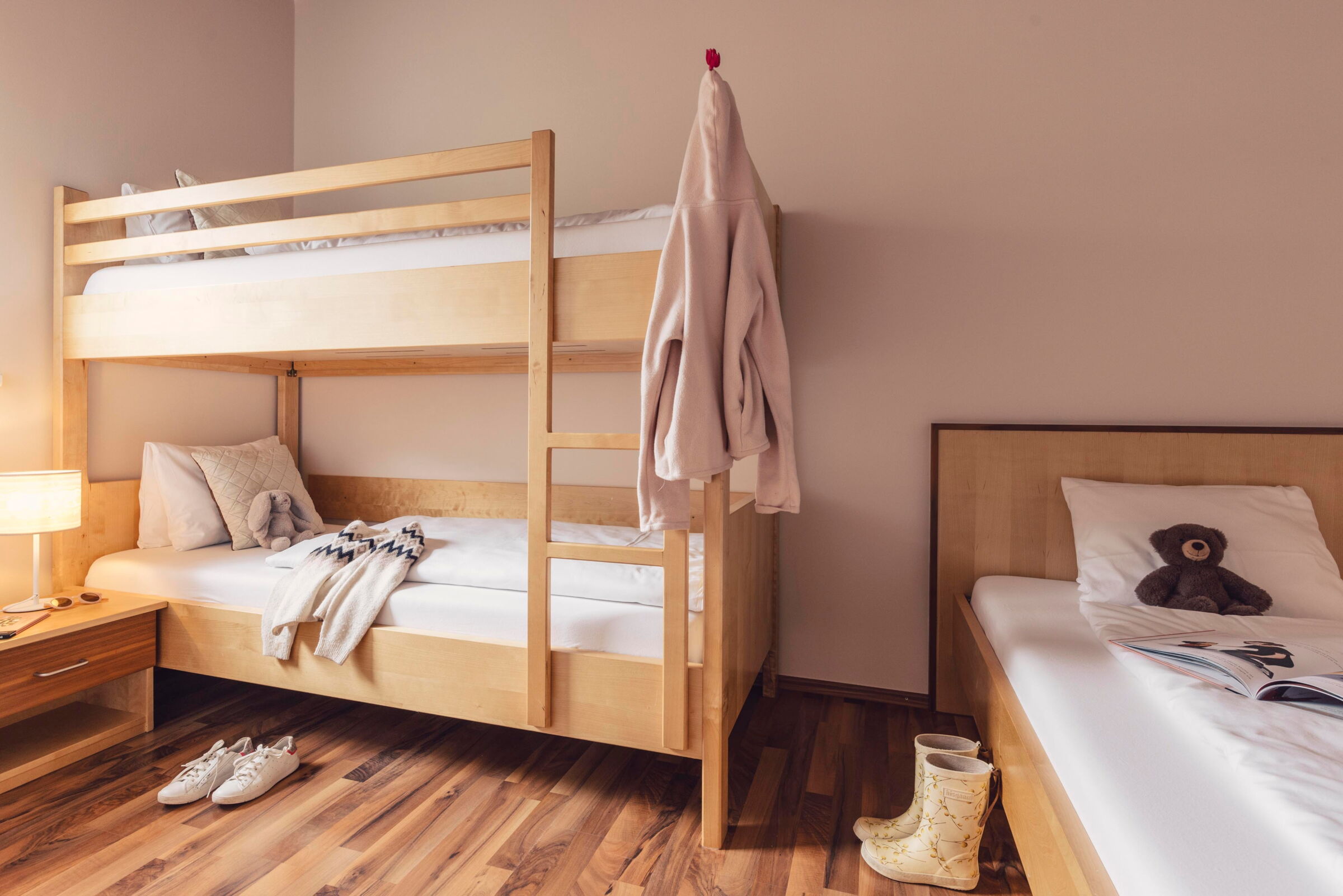 Kinderzimmer mit Etagenbett, Einzelbett, Kuscheltier und gemütlicher Beleuchtung.