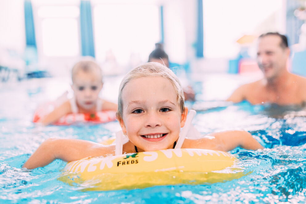 Kinder lachen im Pool, während sie in leuchtenden Schwimmringen planschen.