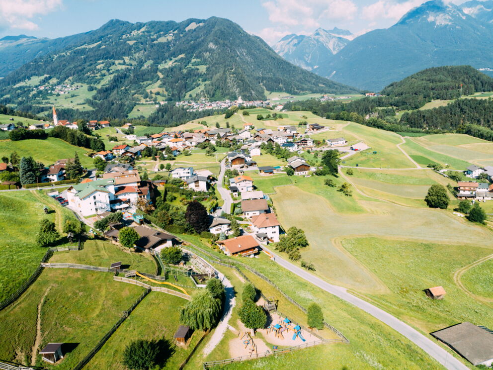 Idyllisches Dorf mit bunten Häusern, umgeben von grünen Hügeln und majestätischen Bergen.