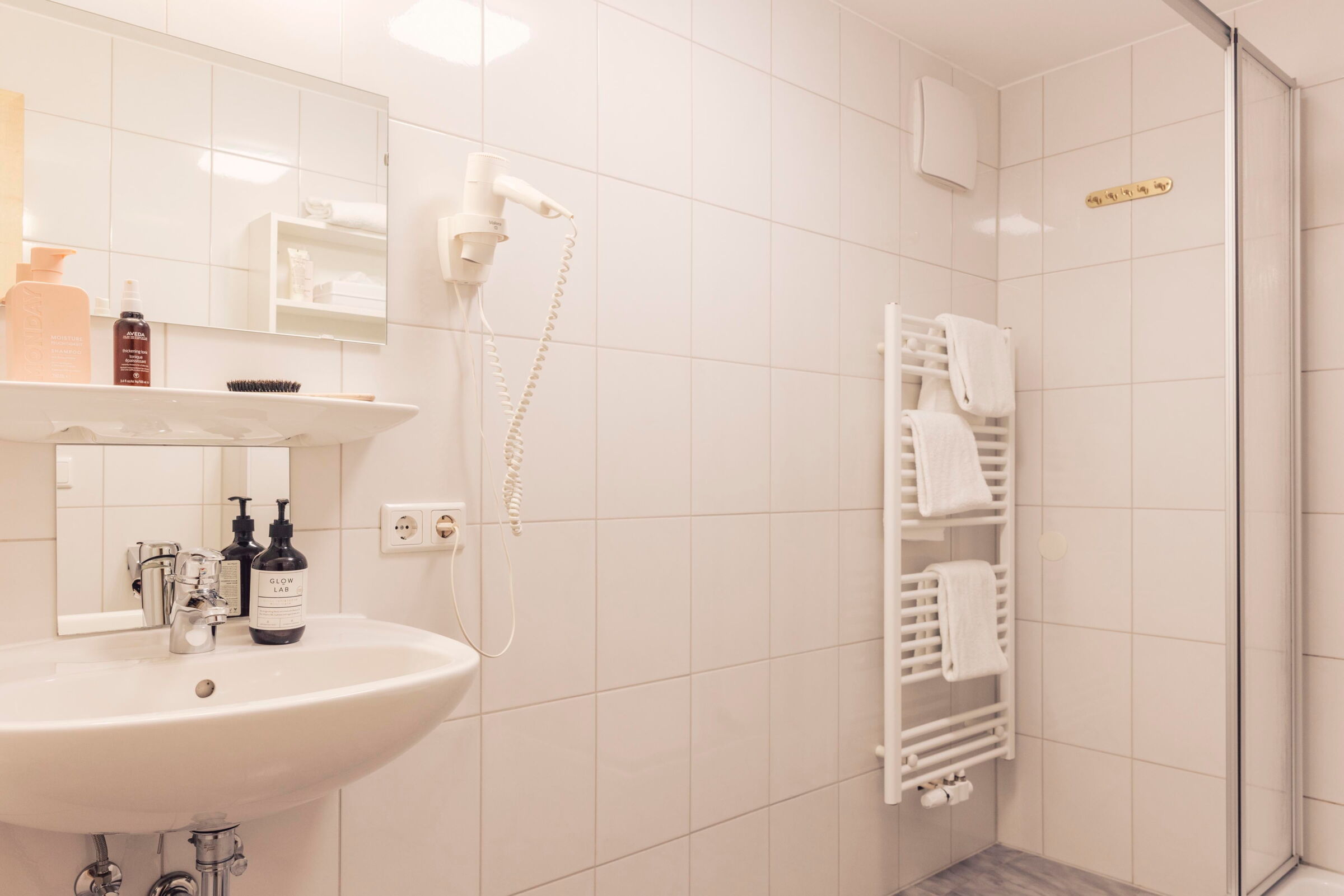 Helles, modernes Badezimmer mit Waschbecken, Spiegel, Handtüchern und Haartrockner.