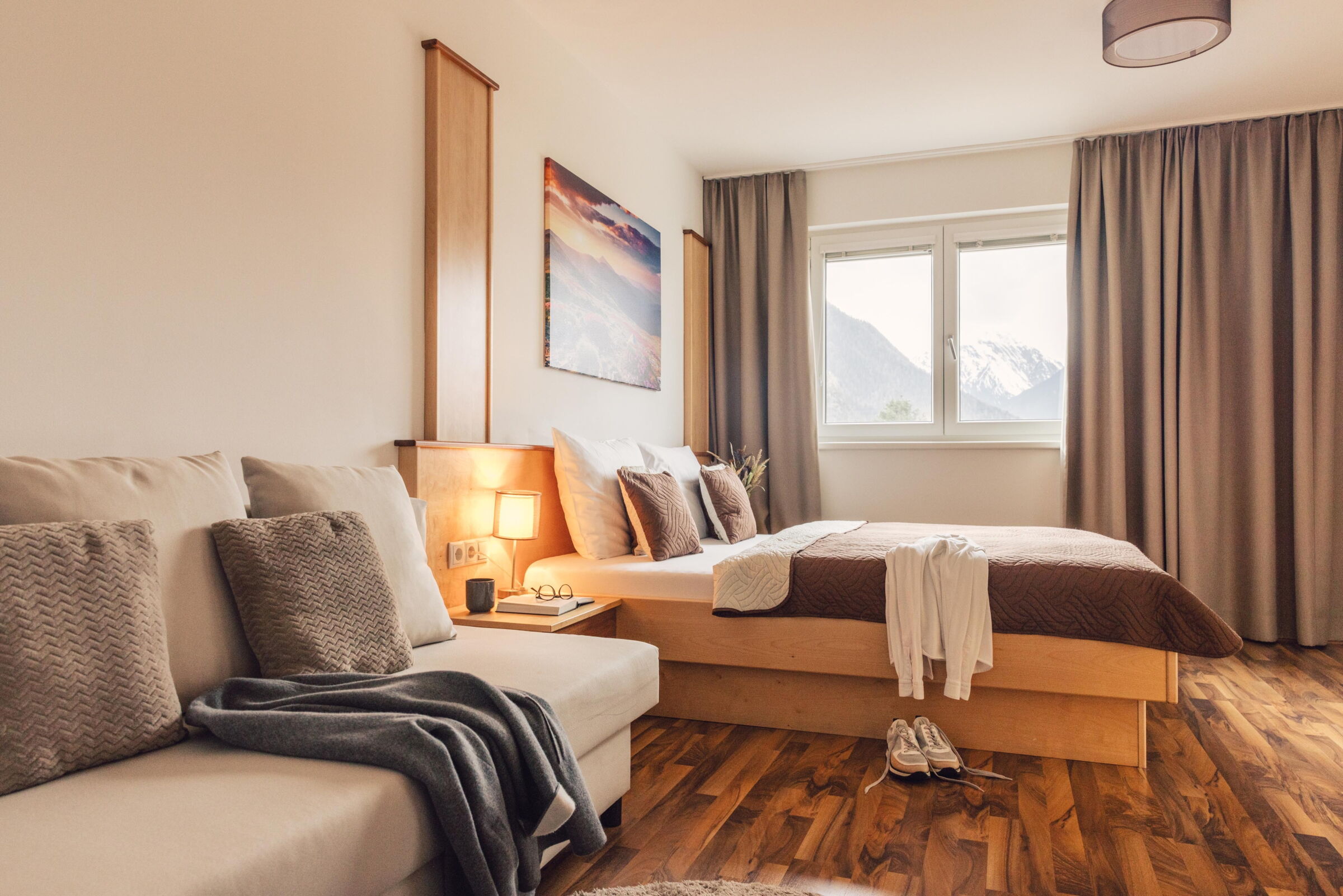 Bright room with comfortable bed, sofa, lamp and window with mountain view.