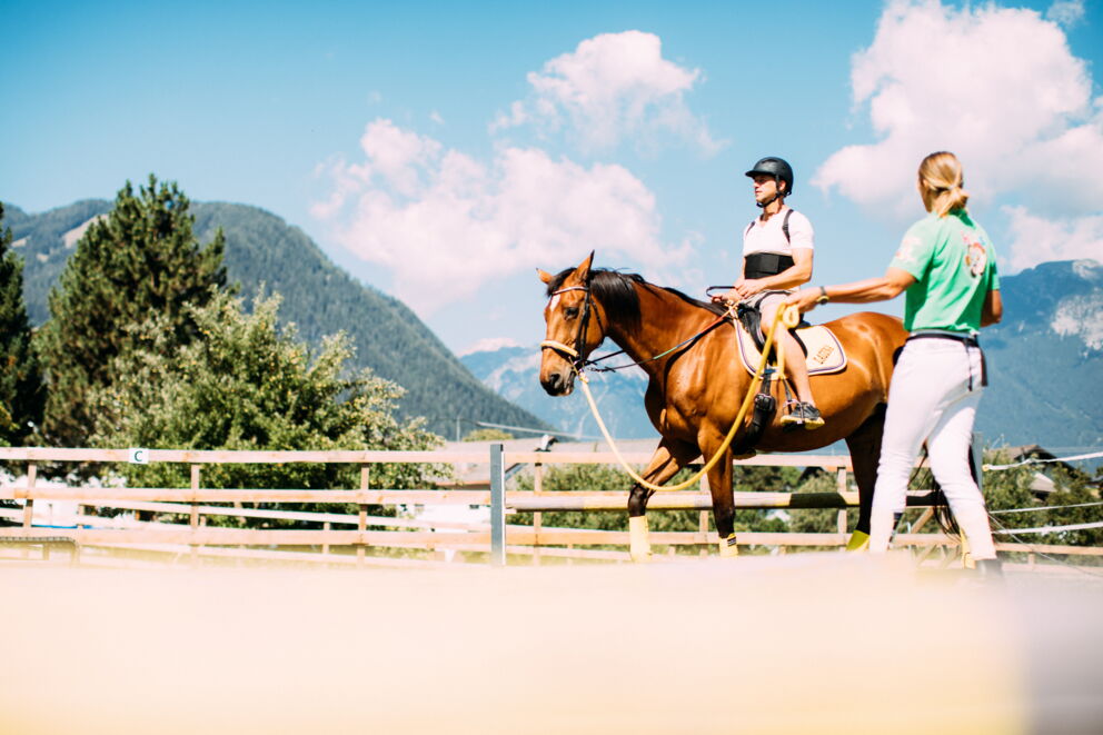 Person riding a horse, surrounded by picturesque mountains and clear skies.