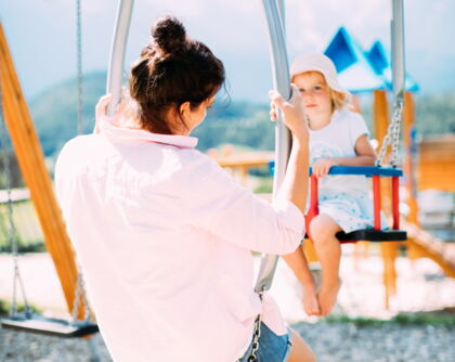 Erwachsene und Kind schaukeln gemeinsam auf einem Spielplatz mit Bergblick.