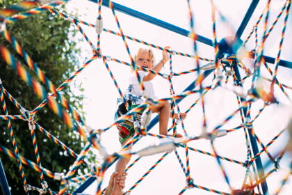 A child climbs laughing on a colorful climbing frame in the sunshine.