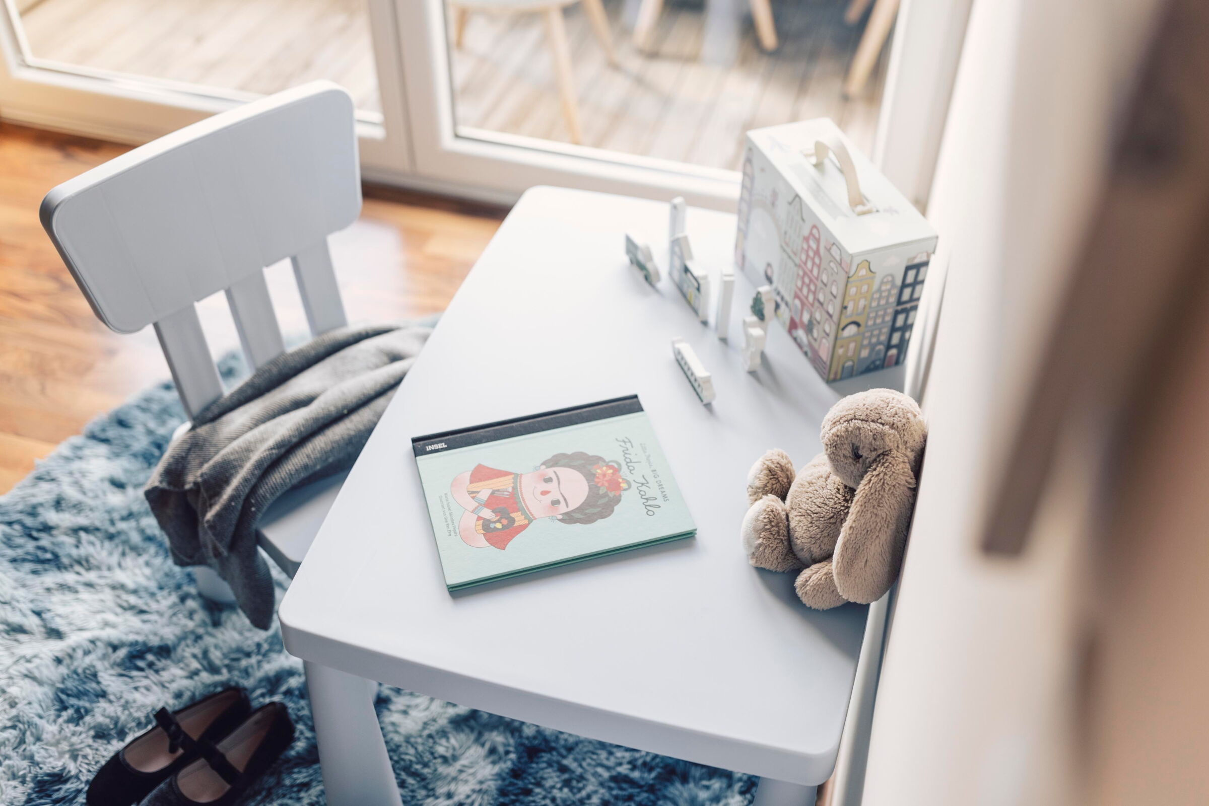 Kindertisch mit Malbuch, Stiften und Plüschtier auf weichem Teppich.