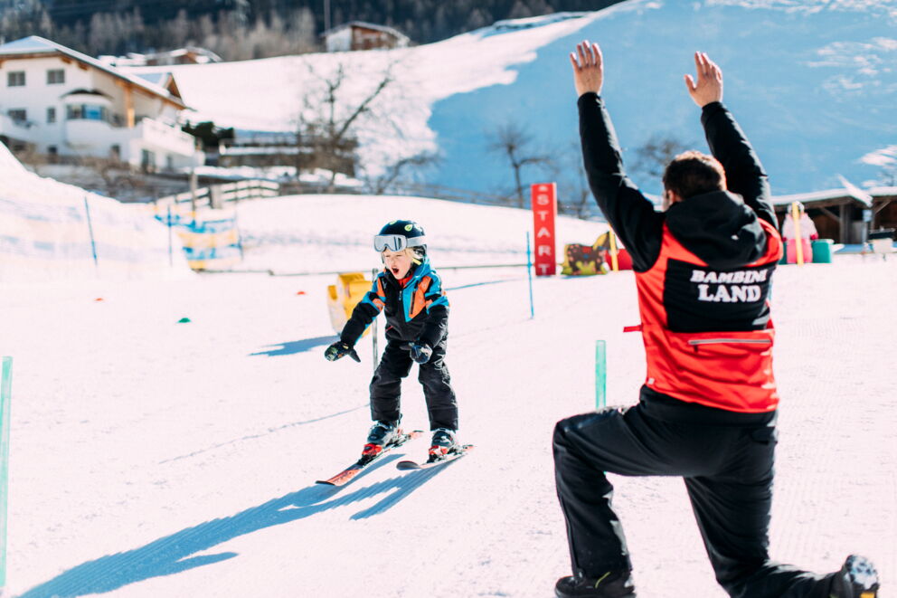 Child learns to ski with an instructor in the snow against an alpine backdrop.