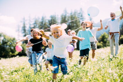 Children and adults run with balloons on a sunny meadow.