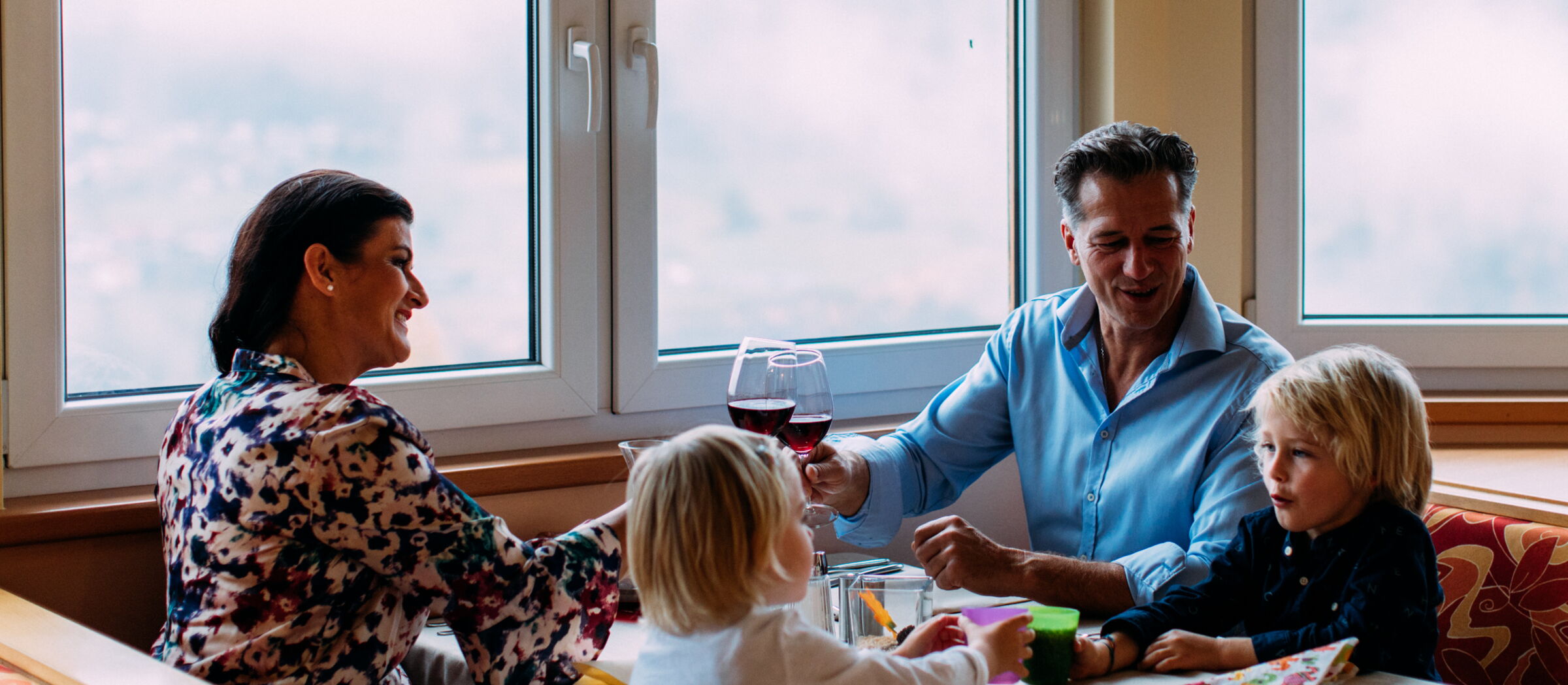 Family enjoying a meal together in a warm, bright dining room with large windows.