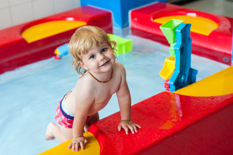 Kleinkind am bunten Wasserspielplatz im Kinderhotel in Tirol.