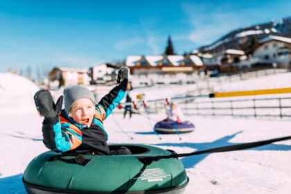 Kind genießt fröhliches Snowtubing im sonnigen Winterwunderland Tirol.